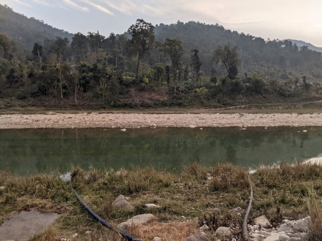 Photo showing a hill landscape in Nepal, with a river running through it and water pipes in the foreground