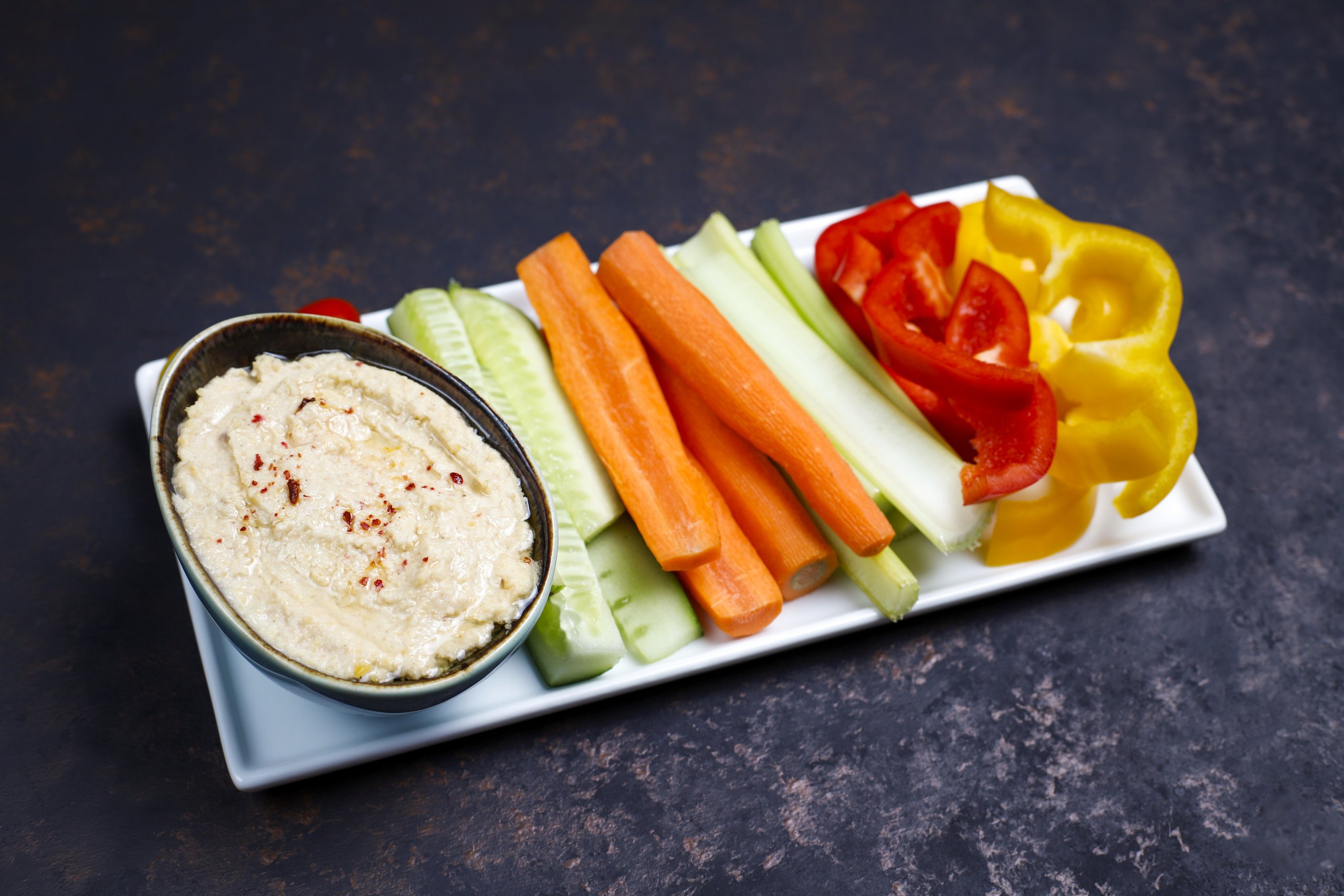 Plate of fresh organic vegetables salad with hummus on dark brow