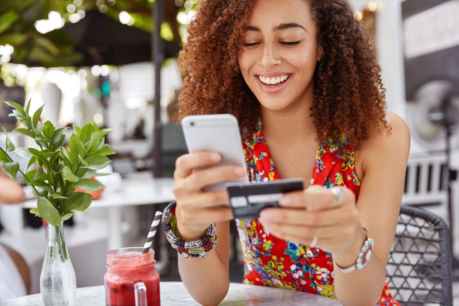 beautiful-dark-skinned-young-female-with-cheerful-expression-holds-smart-phone-credit-card-banks-online-makes-shopping-while-sits-against-cafe-interior.jpg