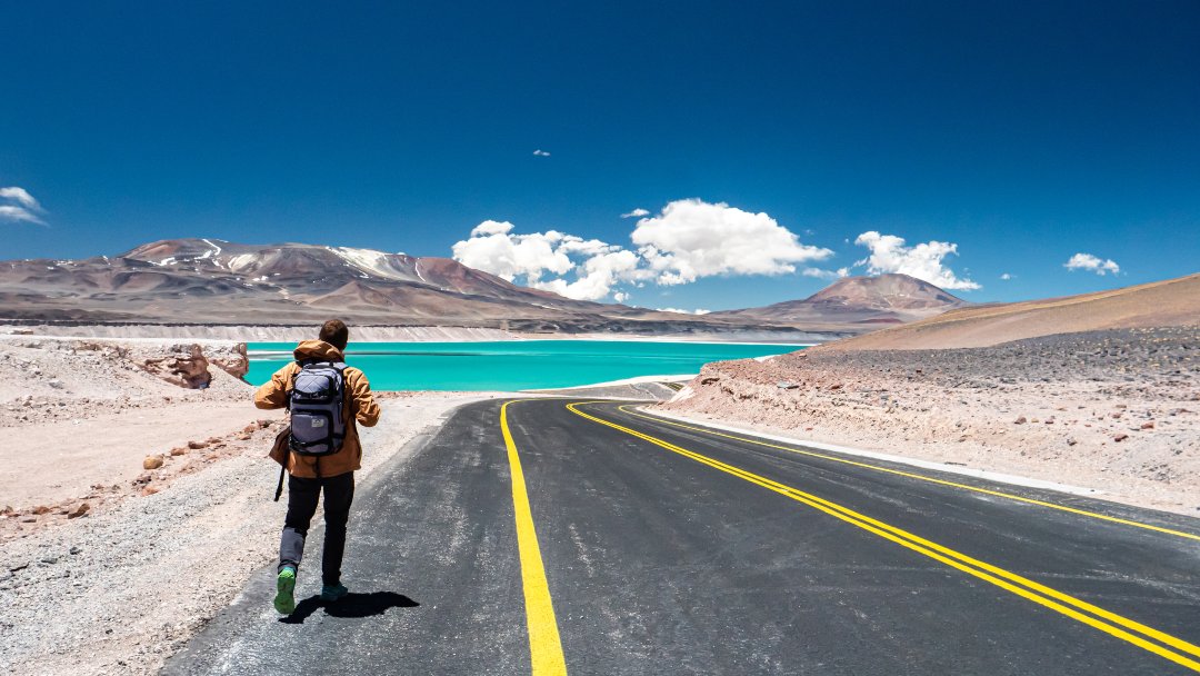 hombre en el camino con montañas y laguna cristalina de fondo