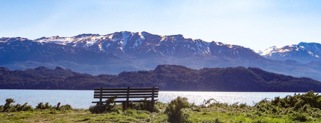 Imagen de una banca de madera, que mira hacia el lago y las montañas, en medio de la Patagonia chilena.