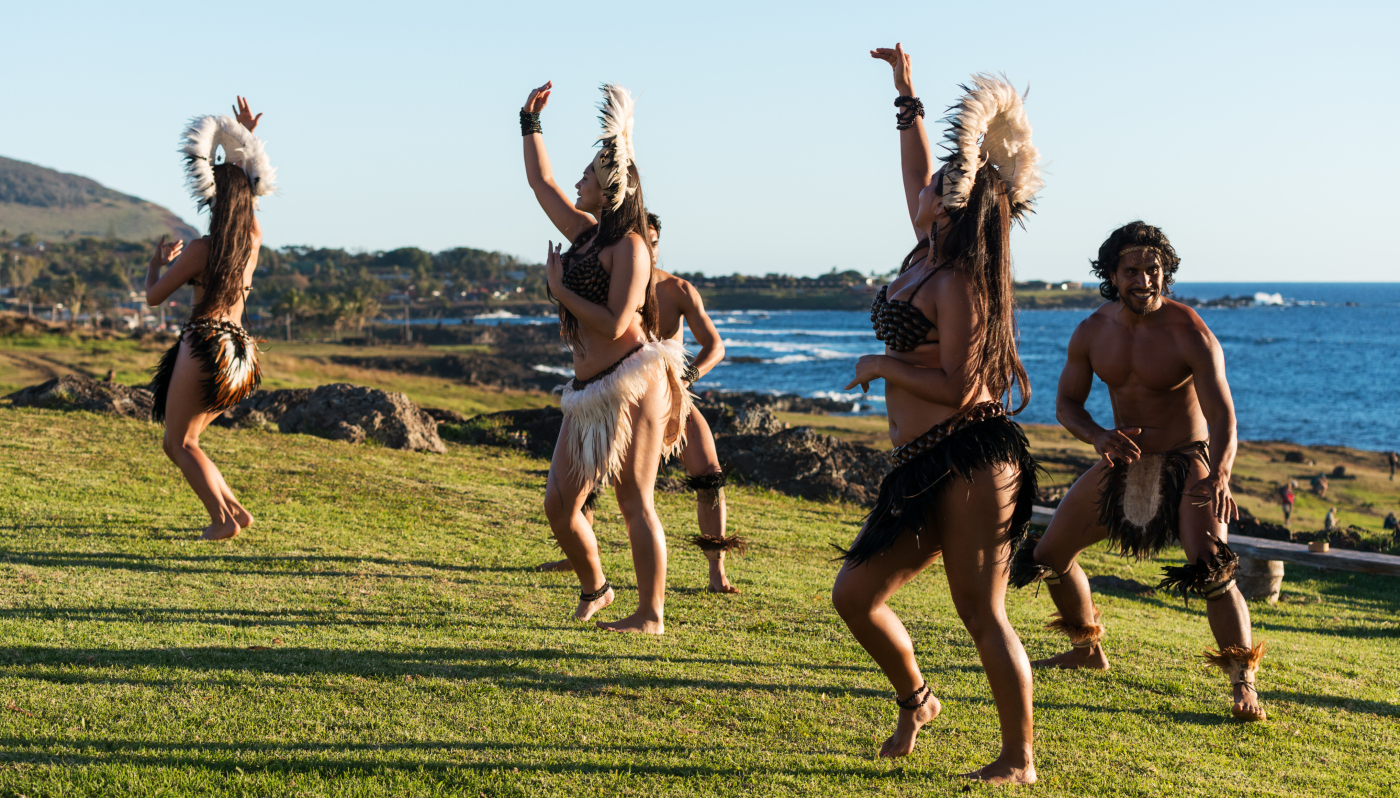 Imagen que muestra a un grupo de bailarines con trajes típicos de los pueblos originarios de la isla de Rapa Nui bailando a la orilla del mar.