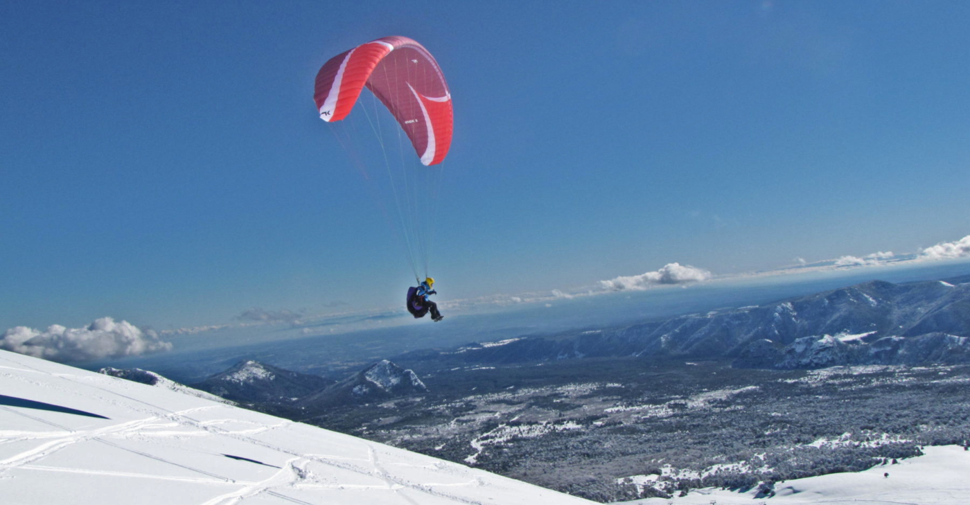 Imagen del vuelo en parapente de un deportista en las cumbres nevadas que rodean el Centro de Ski Las Araucarias