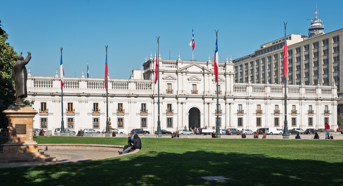 Imagen del Palacio de La Moneda en un hermoso día soleado donde destacan banderas chilenas que la rodean