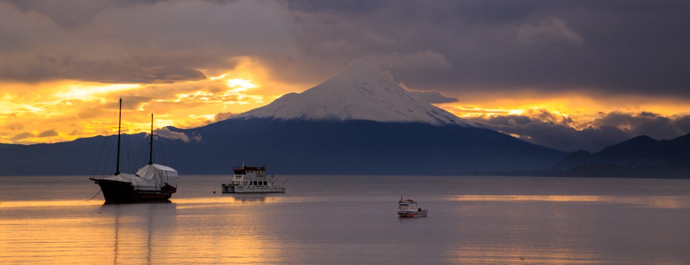 Impactante imagen de navegaciones en medio de las aguas del extremos sur de Chile en una puesta de sol donde destacan las montañas nevadas de fondo