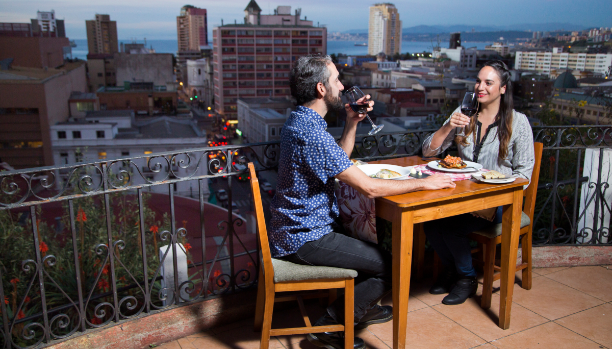 Imagen de una pareja disfrutando de una copa de vino y gastronomia chilena en una terraza de Valparaíso