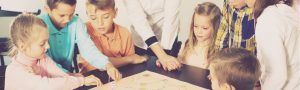 Teacher and happy children with students sitting at table with board game and dice in school