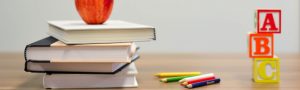 apple on a pile of books with some crayons and letter cubes next to it