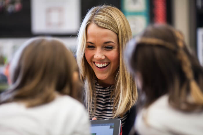 teacher smiling talking to two students with their laptops