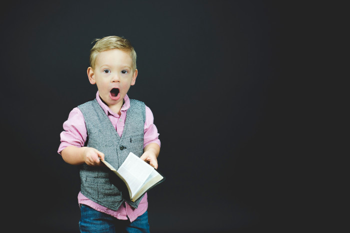 boy with grey vest and pink shirt holding a book