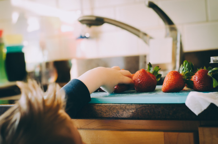 Kid reaching for strawberries on the kitchen counter