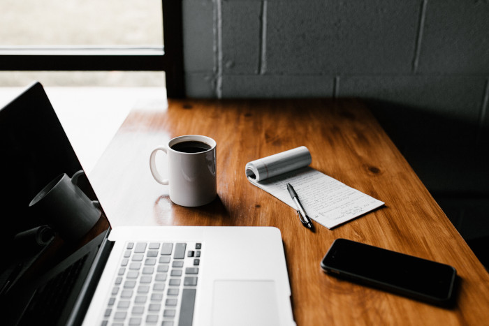 laptop with coffee mug and a notepad on a wooden table