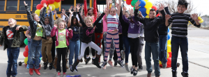 Students jumping in the air outside, beside a bus with balloons