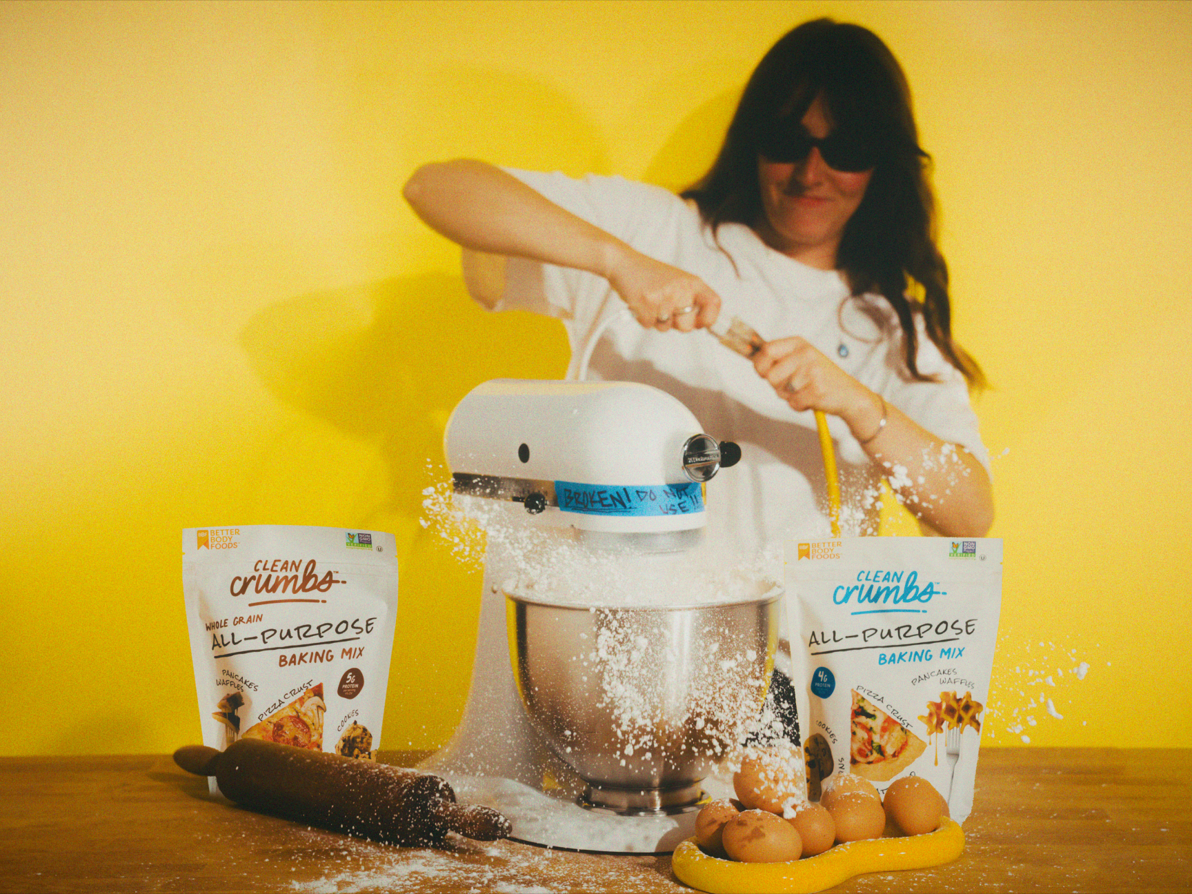 A baker mixing Clean Crumbs baking mix at a stand mixer with product bags and ingredients on the counter
