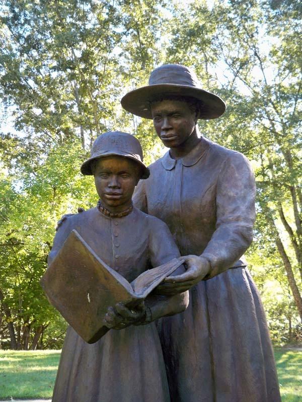 This statue depicts a woman helping a child read.