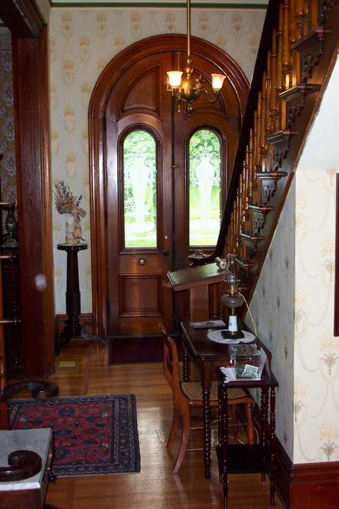A view of Benton House's foyer, within its tower entrance, to include period furnishings, hardwood floors, and its central staircase.