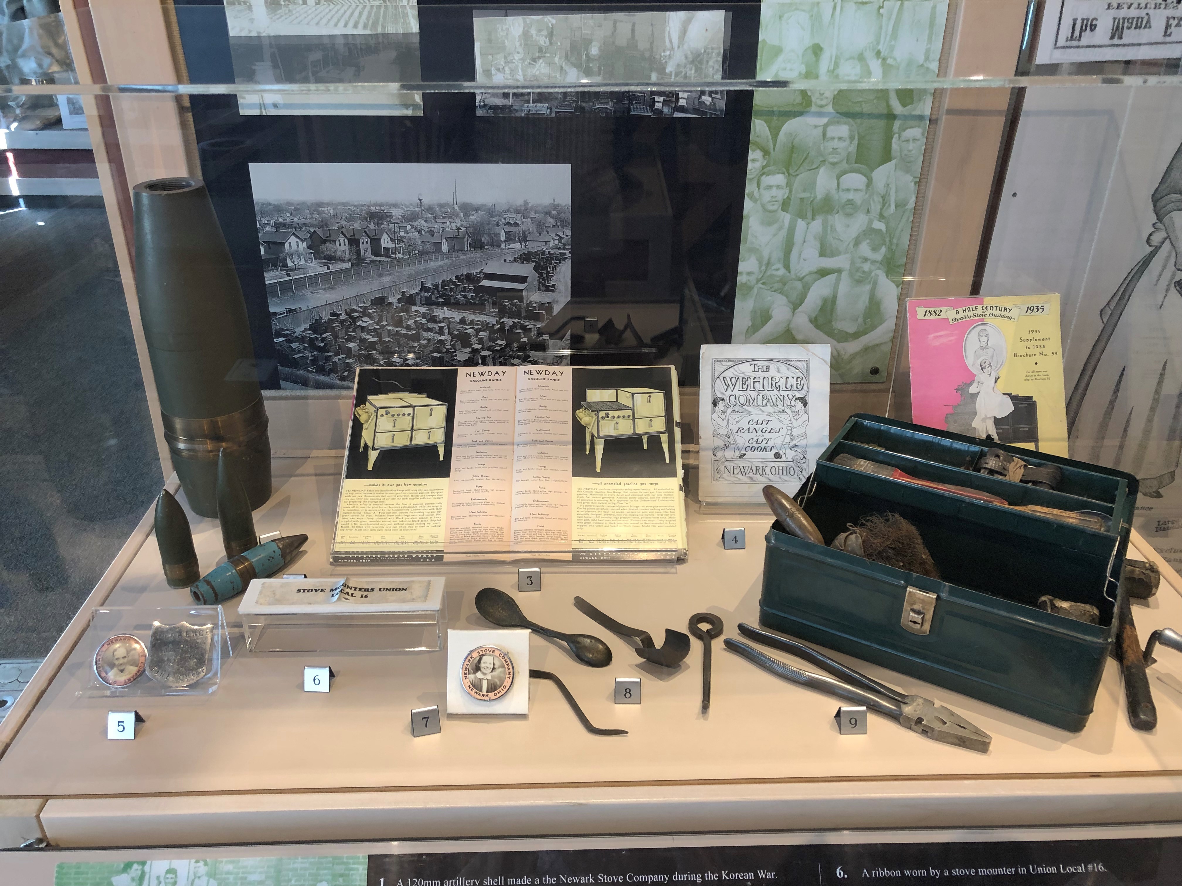 This case displays a variety of objects, including artillery shells made at the Newark Stove Company, employee ID badges, and tools used by workers.