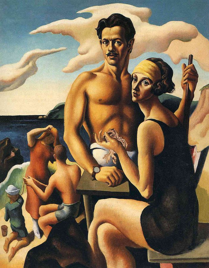 Thomas Hart Benton stands on a beach in front of the ocean. Rita Benton sits next to him. People play in the background.
