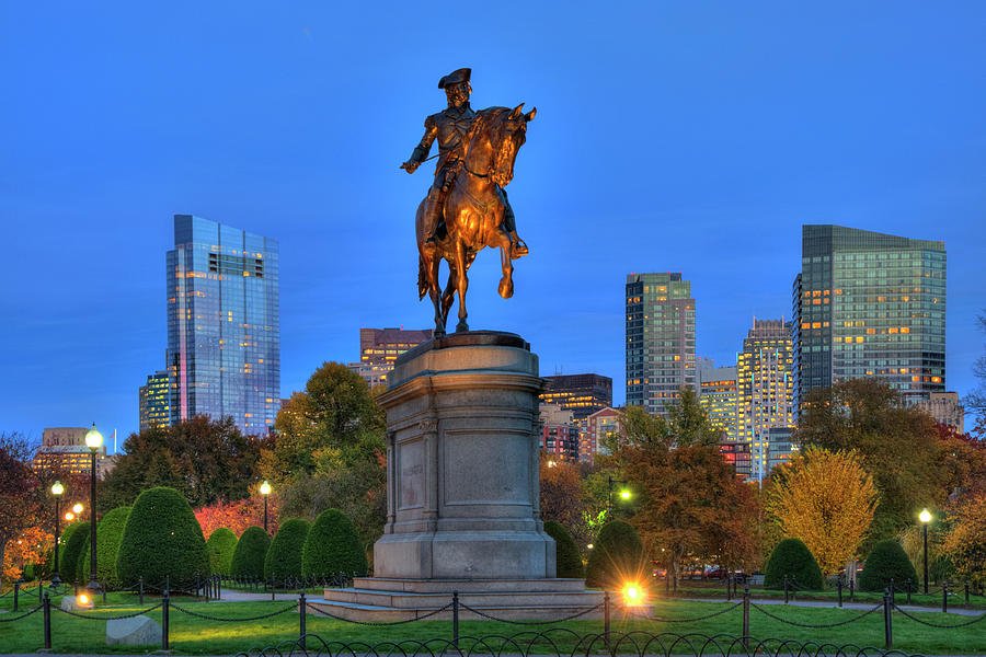 The statue lit up at night against a background of skyscrapers.