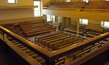 Elevated view of interior, taken from the balcony of the meeting house, with pews on the floor and on risers below.