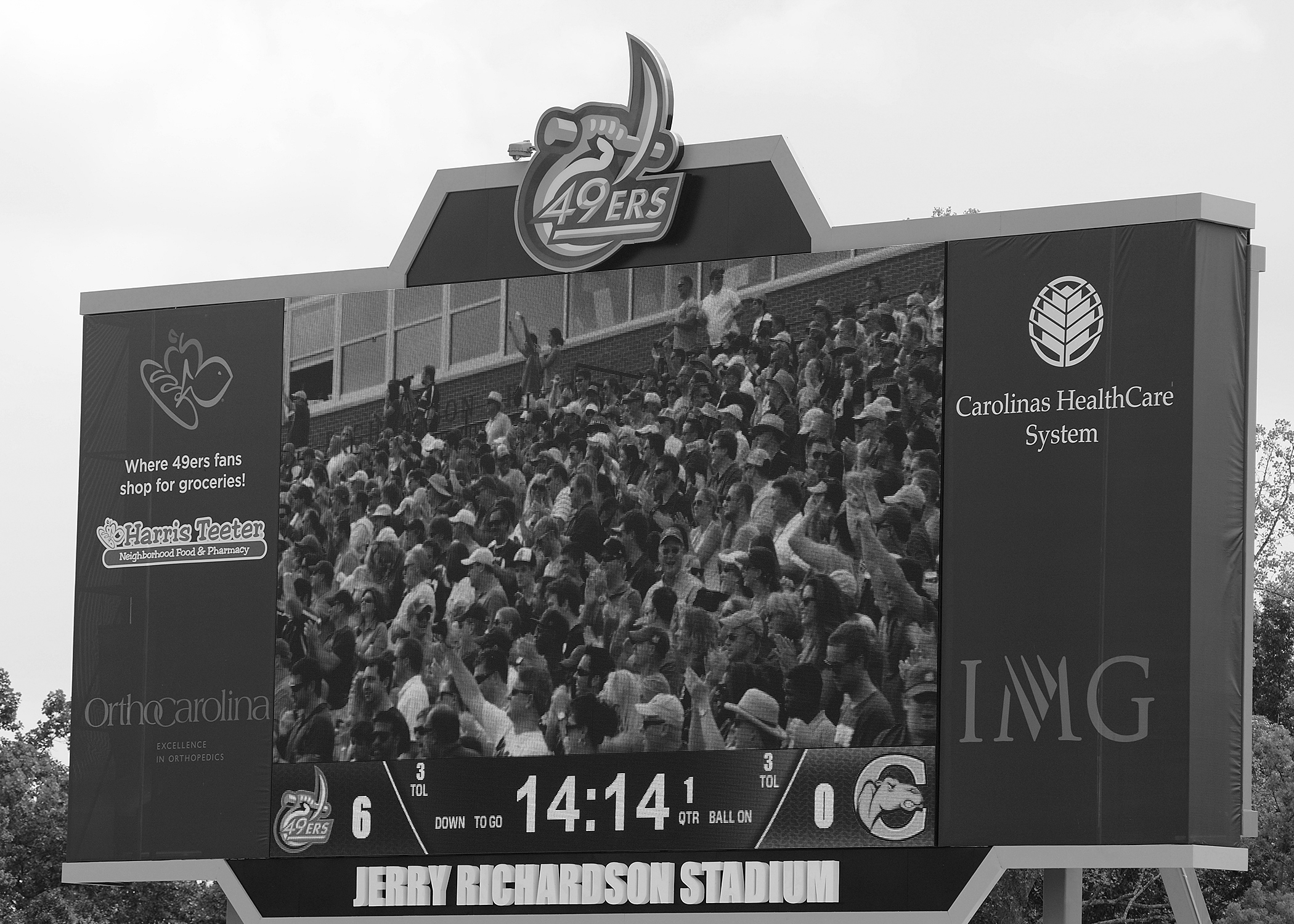 The scoreboard with a screen that shows the crowd in the stands, the score, and sponsors.