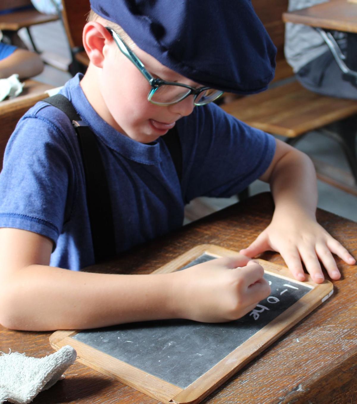 Student writing on slate at their desk during schoolhouse lesson