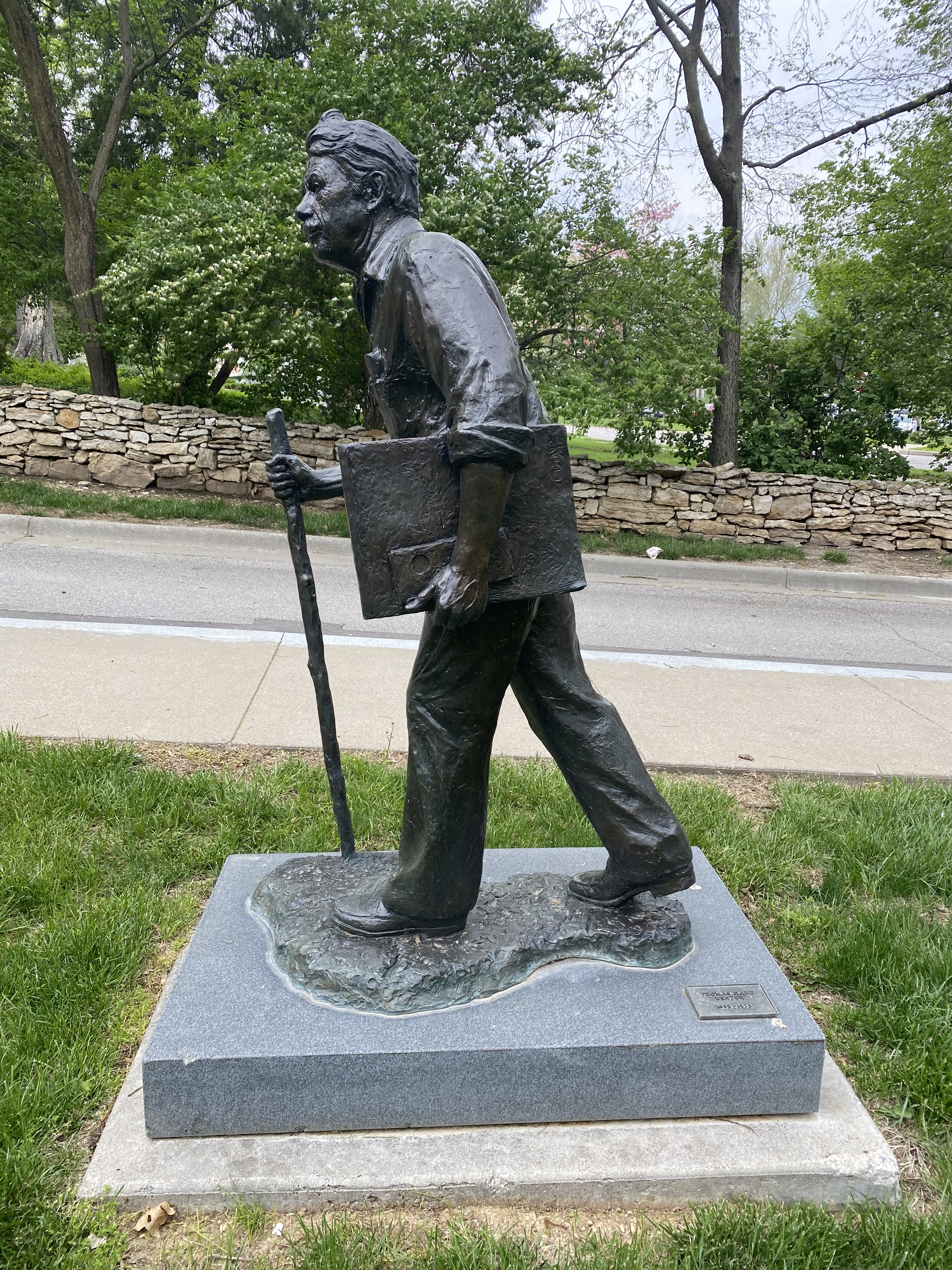 A statue of Benton. He is holding a sketch book and waling with a walking stick.