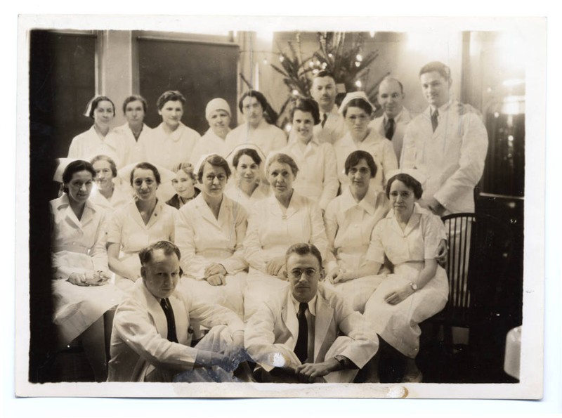 A sepia photograph of the Doernbecher Memorial Hospital for Children staff with Grace Phelps seated at center. Staff are in clinical uniforms. In the background, a Christmas tree is visible.