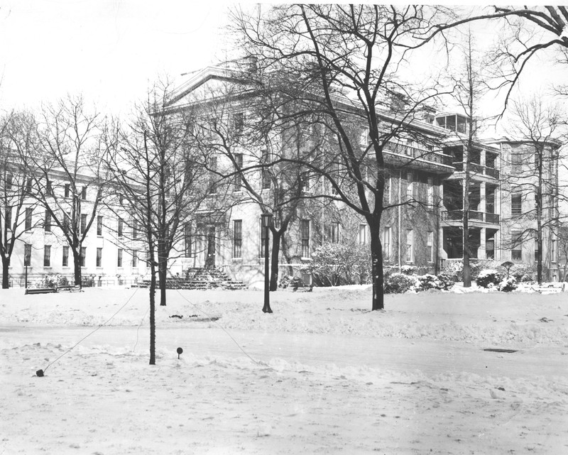 1930 photo of Infirmary building in the background behind trees.