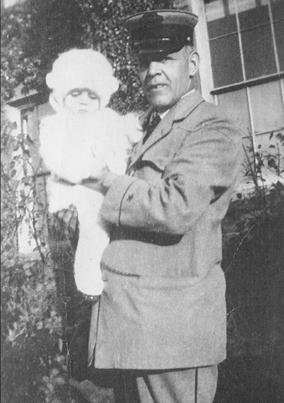 Black and white photo of a man in a suit holding a small child dressed all in white