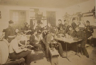 Sepia toned photograph of soldiers sitting in a room cleaning and repairing their equipment