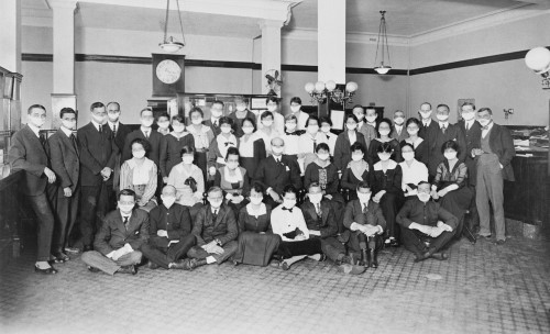 Black and white image of large group of people wearing white face masks