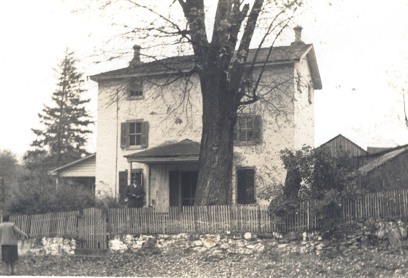 Black and white photograph of the Miller's House showing it covered in stucco and with a third story and a front porch.