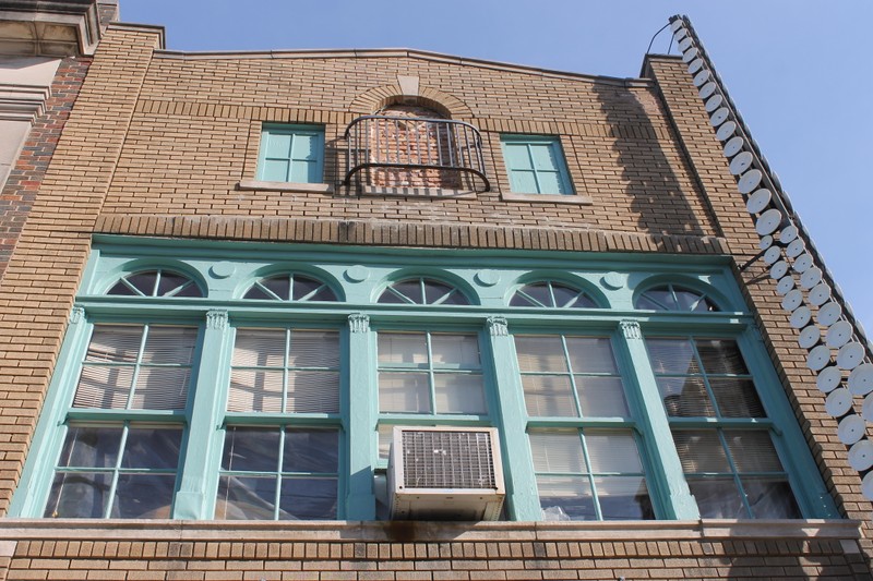 The upper two floors of a three story building built with sand-colored brick. This view shows the distinctive semi-circular windows on the  front of the building, which have cyan frames.