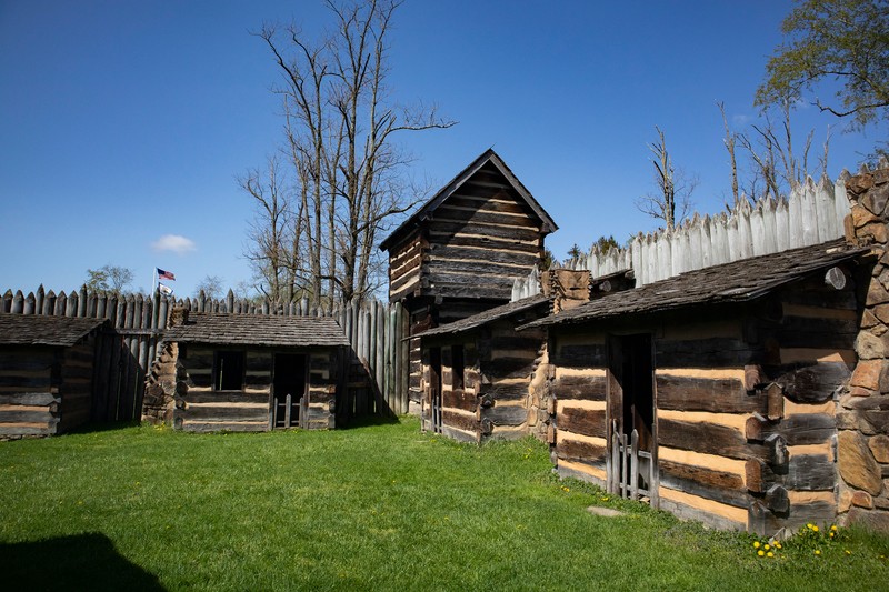 Three small, one-room cabins are visible in this image, along with one of the blockhouses. The cabins have a window or two and open door. The sky is bright blue.