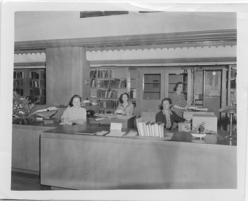 Black and white photograph of library staff at the circulation desk in the Old Library. From left to right: Bertha Brandon Hallam (Librarian), Margaret Hughes, Ora Goodman and Lolita McElveny.