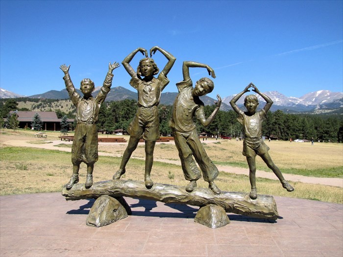Four children standing on a large log are depicted in this bronze sculpture spelling out the letters "Y", "M", "C", and "A" with their arms. The child on the far left is wearing clothes from 1907, when YMCA of the Rockies was founded. The other children are wearing clothes to represent other years throughout the history of the organization.