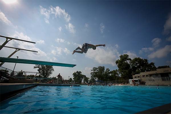 A child flies through the air above a diving board and swimming pool.