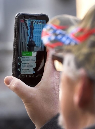 Man from Heirs to the Confederacy in a confederate-themed hat by the name of Howard Snow is seen recording the removal of the statue. Angry responses are shown on his phone.