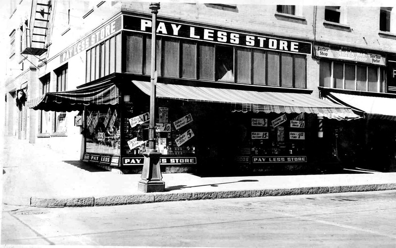 The Olympia Hotel building at the northwest corner of Palouse Street and North Wenatchee Avenue cira 1935.  Facing Wenatchee Avenue are the following business: Pay Less Store, Andy's Hat Shop, Mirror Barber Shop & Beauty Parlor and a part of Pangborn's Jewelers.