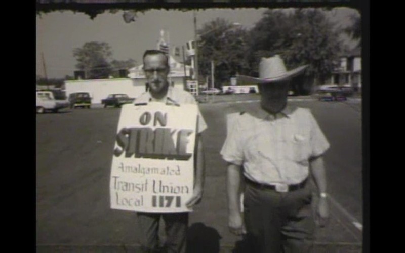 Two employees walking outside of the Ohio Valley Bus Company's bus barn, during the 1971 strike. Employee on left is wearing a sign that reads, "ON STRIKE Amalgamated Transit Union Local 1171"