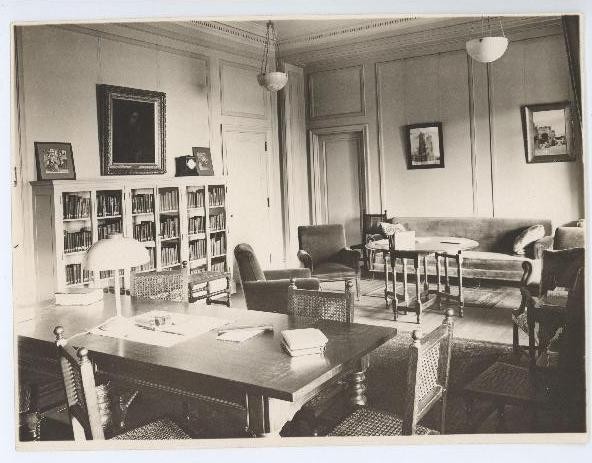 Formal lounge area, desk, table surrounded by chairs, bookcase and sofa.