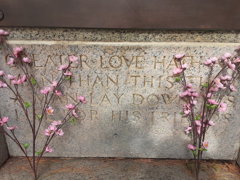 Directly below the bronze plaque: "Greater love hath no / man than this that / a man lay down his / life for his friends / St. John XV, 13"