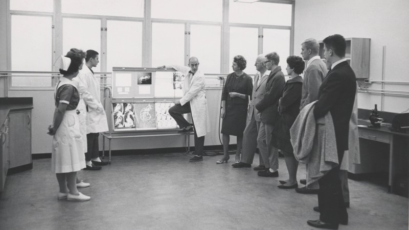 Black and white photograph of Charles T. Dotter, M.D. showing images on a large metal machine to visitors. Includes view of two people in medical uniforms.