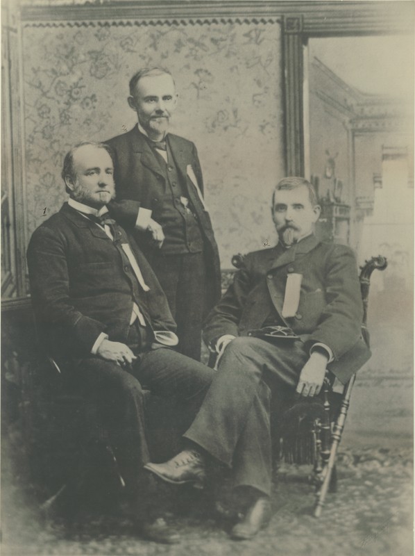 Group photograph: “Three heroes of the Iron Brigade: Lucius Fairchild, [seated left] Edward S. Bragg [standing], and John Gibbon [seated right]”, probably taken during the 1885 Iron Brigade Association Reunion in Madison, WI.  