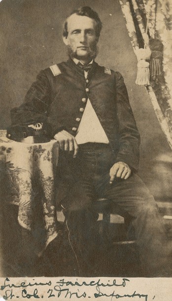 Carte-de-visite full-length portrait photograph of Lucius Fairchild. He is shown seated in uniform with a forage cap resting on a table.