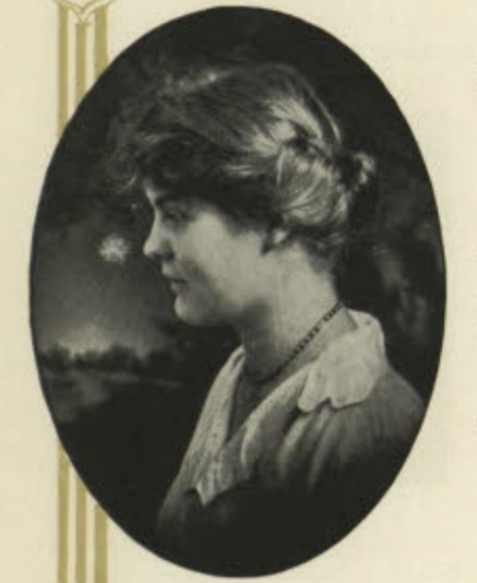 Black & white, profile of a young woman, dark hair rolled off the face. White v-neck collar.