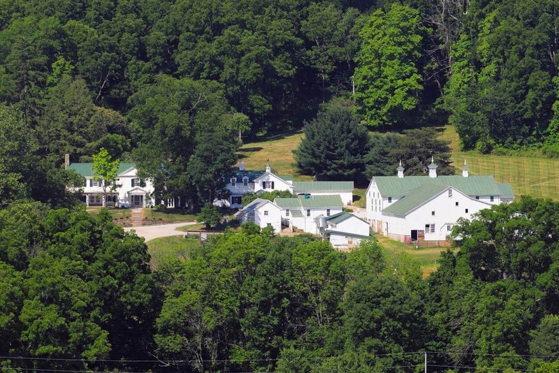 In a lush green valley resides a handful of white buildings with dark green metal roofs.
