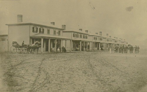 This photograph shows the 5th Infantry Band parading on the streets of Fort Hays, Kansas, in front of the officer's quarters.