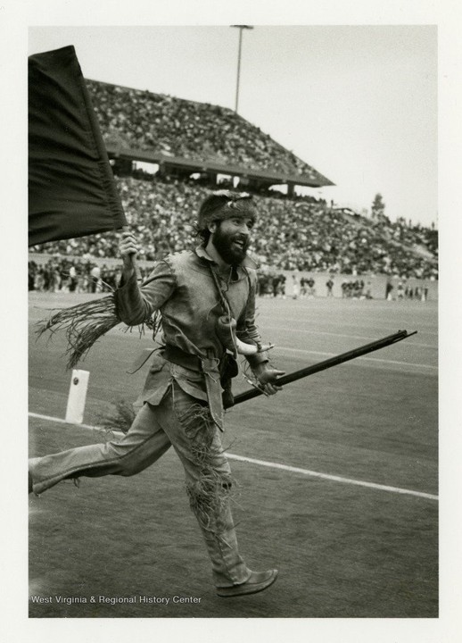 Official Mountaineer mascot Matthew Zervos carries WVU's colors onto the "new" Mountaineer Field, which was then over half a decade old during Zervos's tenure in 1986-1987. West Virginia & Regional History Center.